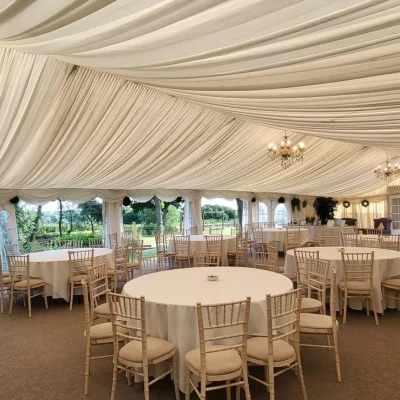 A spacious luxury marquee at Downham Hall Essex filled with round tables, a stage, and professional lighting for a corporate event.