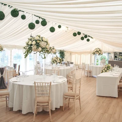 Spacious luxury marquee with white draped ceilings, floral centerpieces, and round tables for large events in Essex.